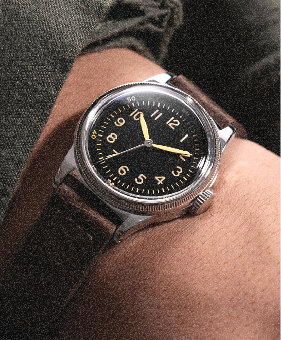 A-11 black dial watch on a brown leather strap, worn on the wrist